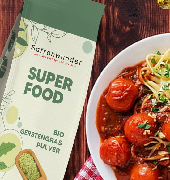 Ein Teller mit Tagliatelle und gannzen Tomaten in einer Soße, neben dran das Bio Gerstengras Superfood von Safranwunder