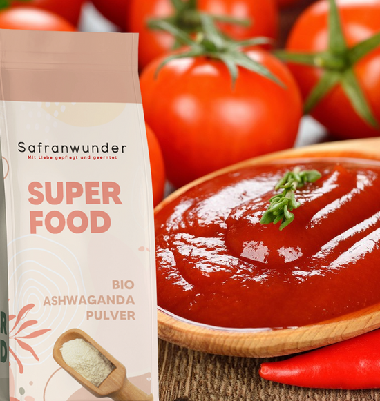 Frische Tomaten und Chillis im hintergrund, im vordergrund ein Holzlöffel mit cremiger Tomatensoße gleich neben dran das Bio Ashwagandha Superfood von Safranwunder